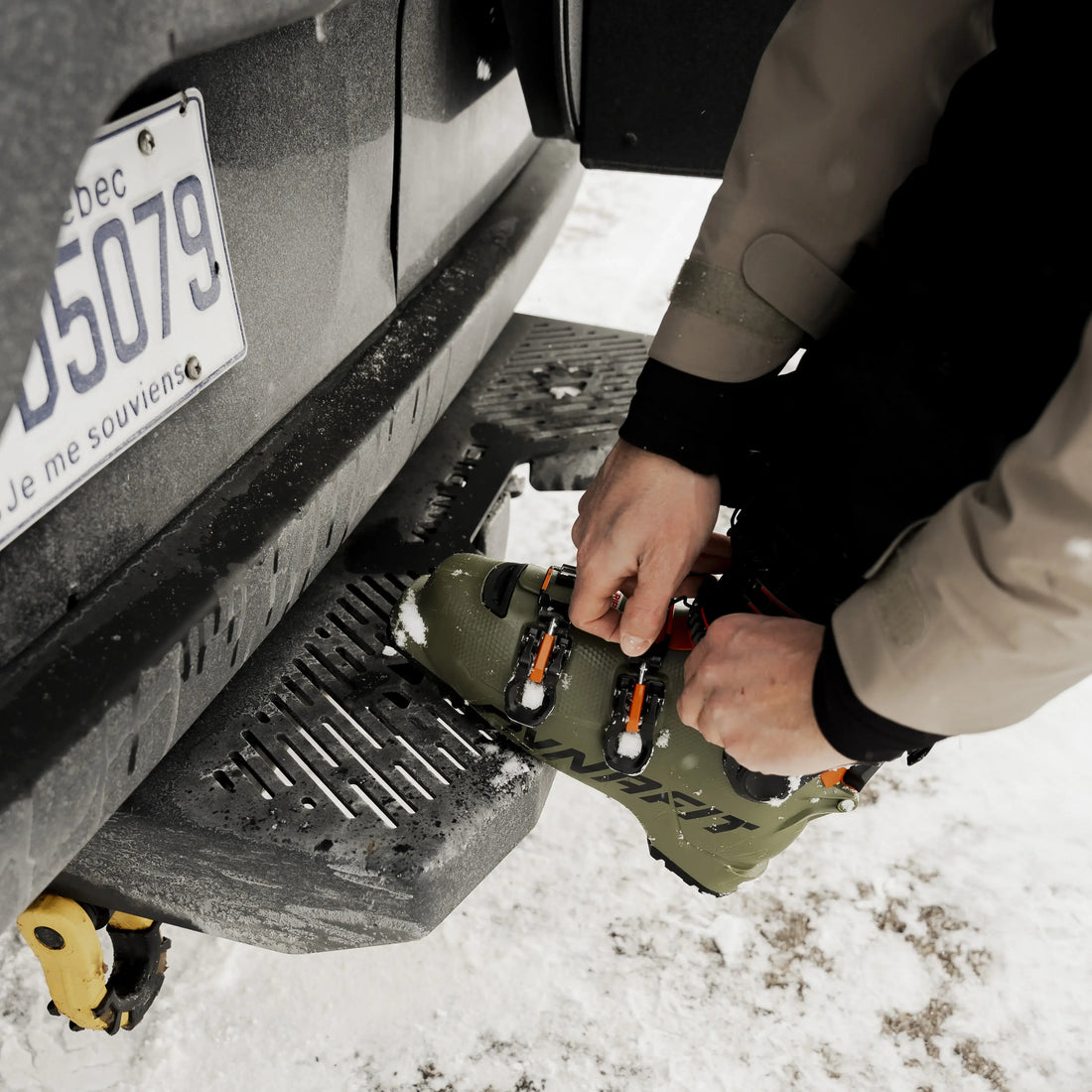 Person using a rear step on the back of a vehicle in a snowy environment